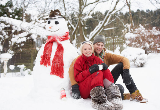 Teenage Couple In Winter Landscape Next To Snowman With Flask An