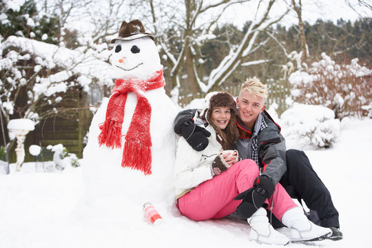Teenage Couple In Winter Landscape Next To Snowman With Flask An