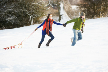 Teenage Couple Pulling Sledge Across Snowy Field