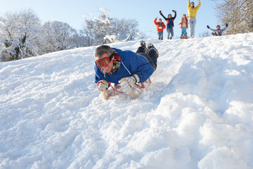 Man Sledging Down Hill With Family Watching