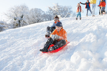 Young Boy Sledging Down Hill With Family Watching