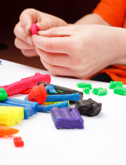 Boy moulds from plasticine on table.