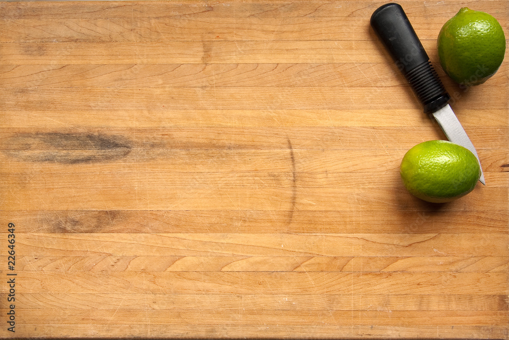 Wall mural limes and a knife sit on a worn butcher block cutting board