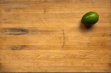 A lime sits on a worn butcher block cutting board