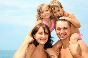 mother and father near water with little girls sitting on necks