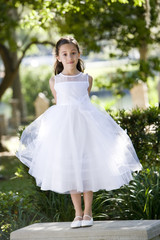 Beautiful child wearing white dress standing on park bench