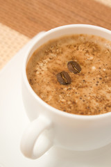 White coffee cup on saucer with two beans floating on surface