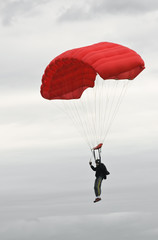 Parachutiste avec parachute rouge atterrissant par mauvais temps