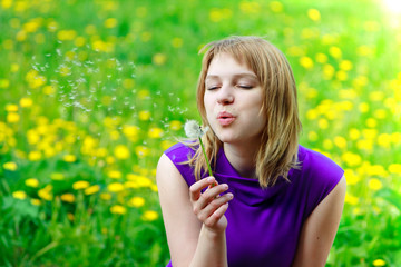 Beautiful woman blowing dandelion on the meadow