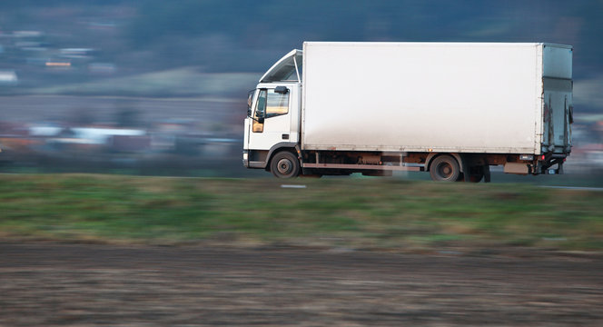 white delivery truck going fast on a road (panned image - motion