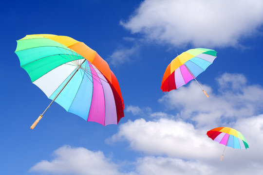 Three rainbow umbrellas flying in a rich blue sky.