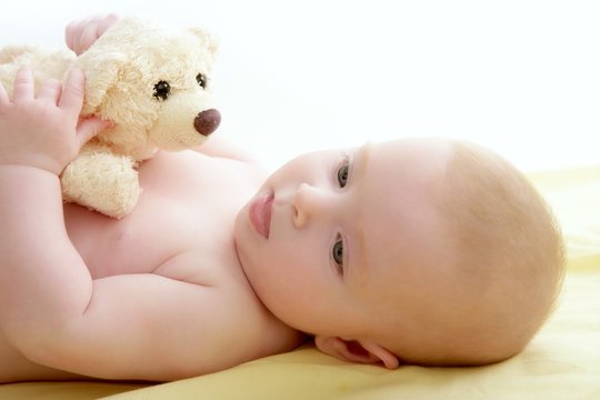 baby playing teddy bear laying on bed
