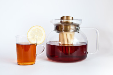 Glass of hot black tea with lemon and a tea pot