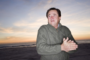 Senior man in sweater at dawn on beach