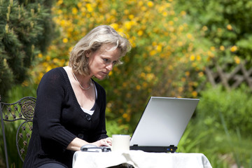 hübsche blonde Frau im Garten arbeitet konzentriert am Laptop