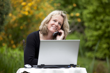 hübsche blonde Frau mit Laptop telefoniert mit Mobiltelefon
