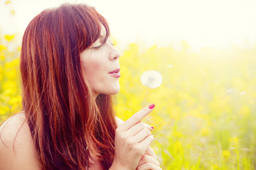 young woman blowing over a dandelion