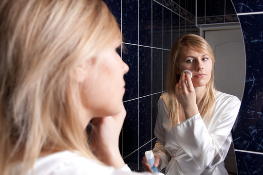 Blond young woman in bedroom applying makeup