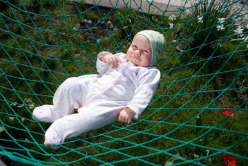 baby in romper suit and skull cap swings in a hammock