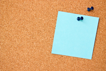 One blue post-it note with blue pushpin on corkboard