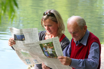 Großvater und Enkelin beim Zeitunglesen im Grünen am Teich