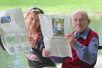 Großvater und Enkelin beim Zeitunglesen im Grünen am Teich