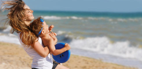 young happy mother playing with son on beach background