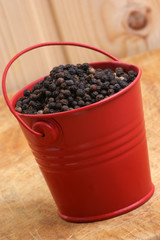 schwarze Pfefferkoerner in einem roten Eimer