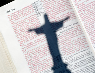 Bible with shadow of open arm Jesus on page of Luke