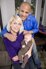Happy parents holding baby sitting on sofa at home