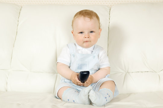 The baby sits on a white sofa with the TV panel