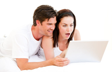 Surprised couple using a computer lying on their bed