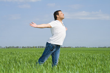 young man moves in a green field of grass to meet the sun