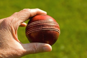 Used red leather cricket ball being held by hand