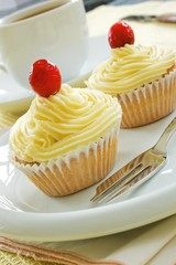 Two buttermilk iced cupcakes on a white plate with a fork