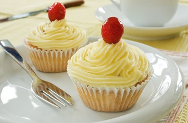 Two buttermilk iced cupcakes on a white plate with a fork
