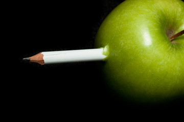 A white pencil inside a green apple on black background