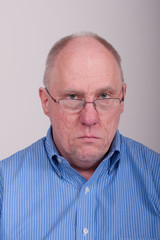 Older Balding Man in Blue Shirt Looking Unhappy Over Glasses