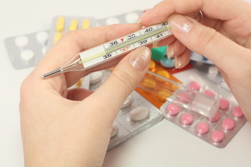 woman's hand holding a thermometer over the pills