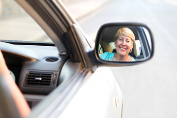 happy senior driving looking in side mirror
