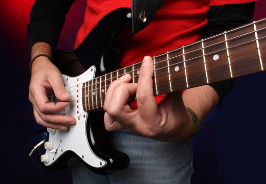 Detail of a musician playing a black electric guitar.