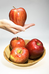 The hand holds an apple and a bowl with red apples