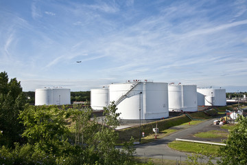 Fototapeta premium white tanks in tank farm with blue sky and aircraft
