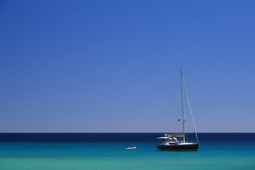 Sailboat on a clear blue sea under a cloudless blue sky