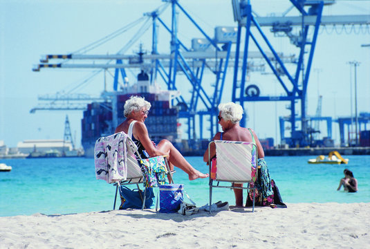 &Auml;ltere Frauen am Strand vor einem Containerhafen