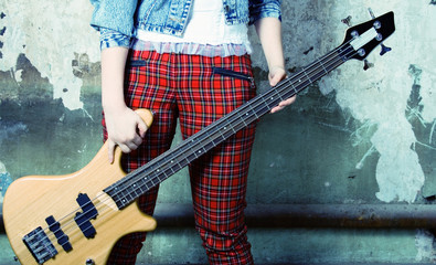 Legs in trousers and a guitar on a background of an old wall.