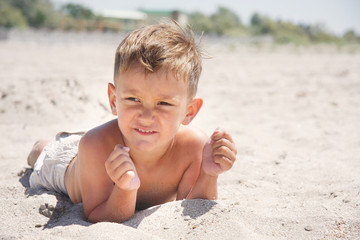young boy laying on sand beach