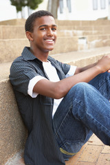 Smiling Male Teenage Student Sitting Outside On College Steps