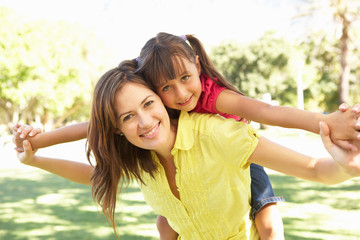 Mother Giving Daughter Ride On Back In Park