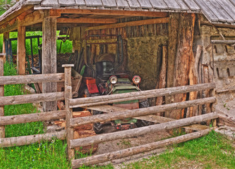 Small old tractor under roof of rustic shed. HDR image